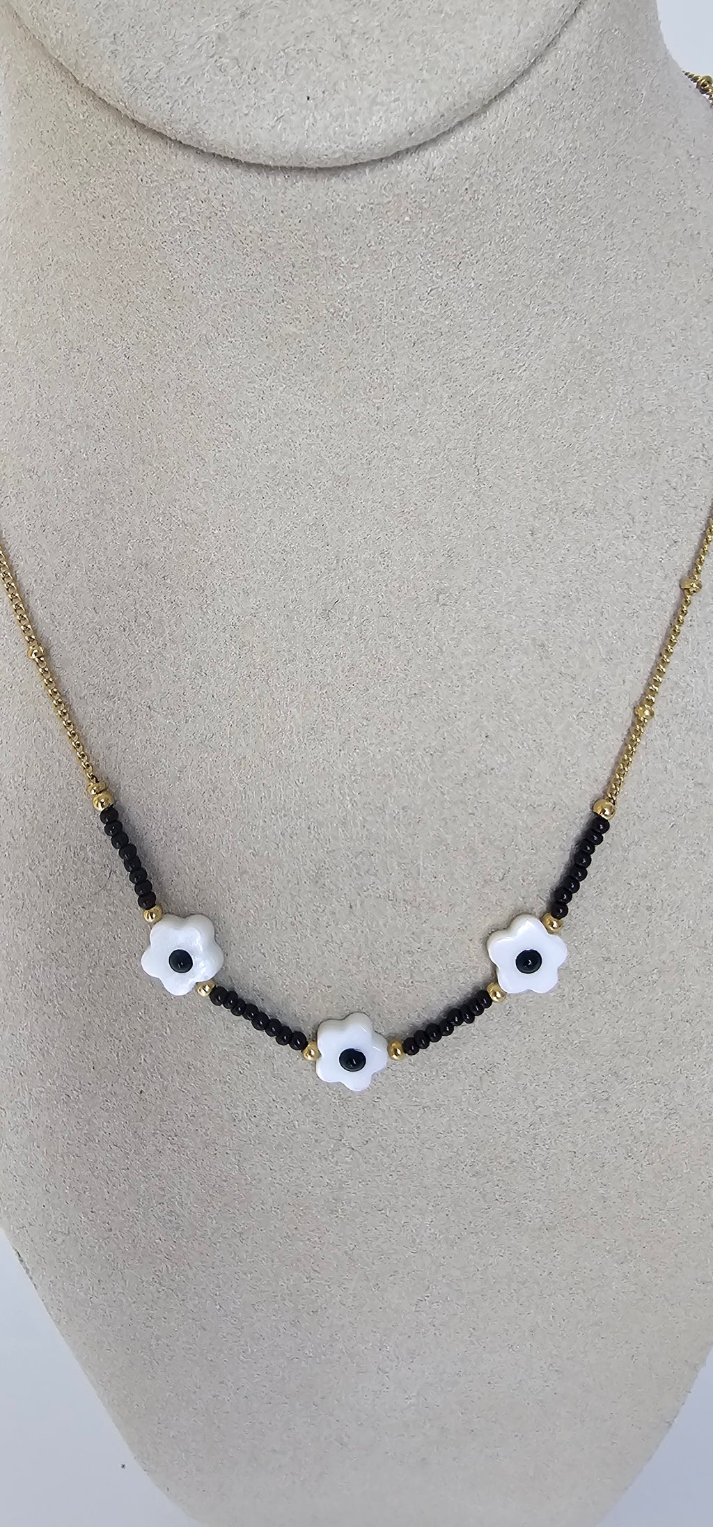 Collier trio fleurs blanches et perles noires sur présentoir doré