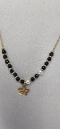 Collier perles noires blanches et fleur dorée sur présentoir