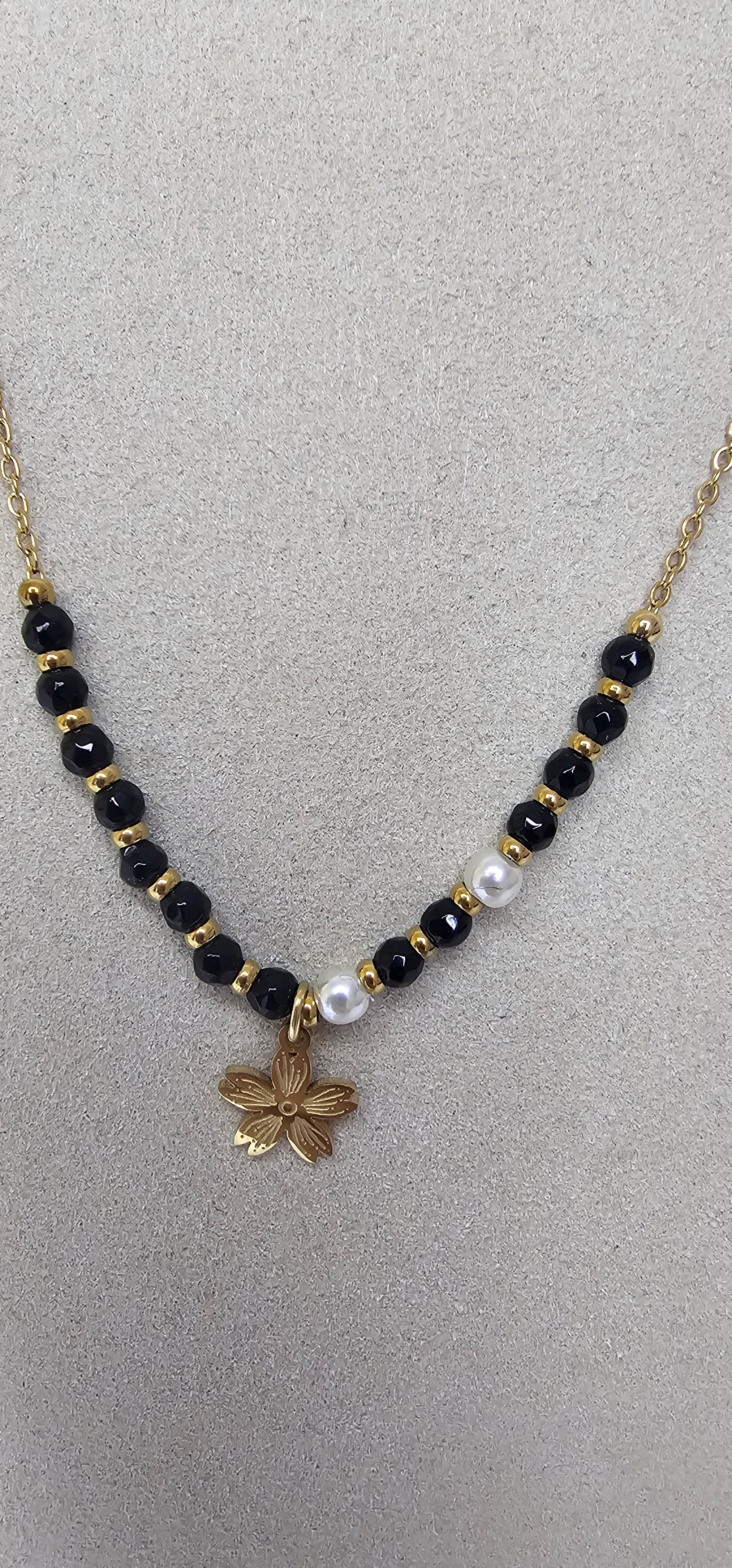 Collier perles noires blanches et fleur dorée sur présentoir